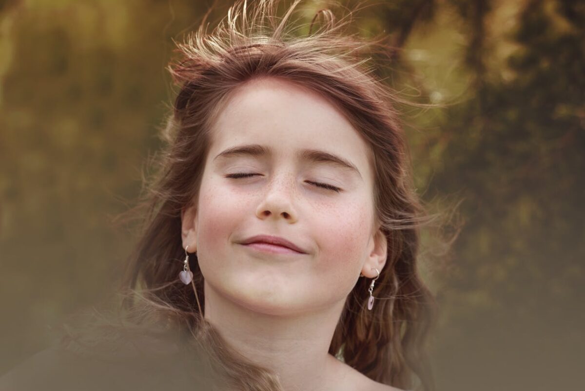 Portrait of a happy girl with closed eyes and wind-swept hair in a natural setting.