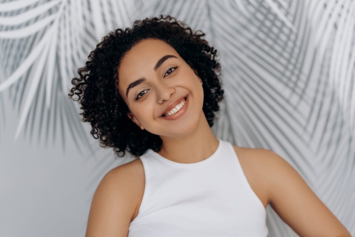 Close-up portrait of a smiling woman with curly hair and a vibrant expression indoors.