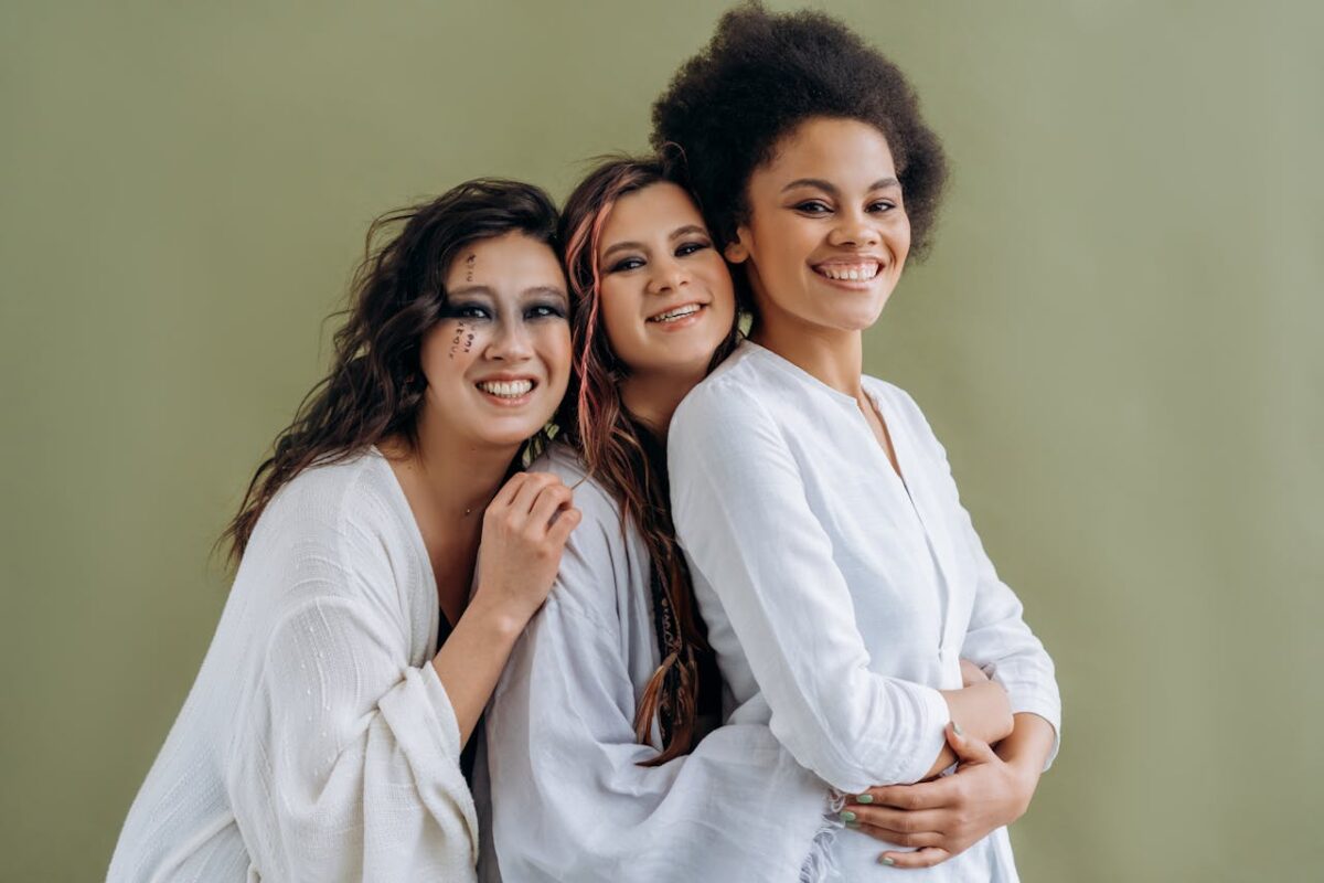 Three diverse women smiling and embracing, symbolizing unity and friendship.
